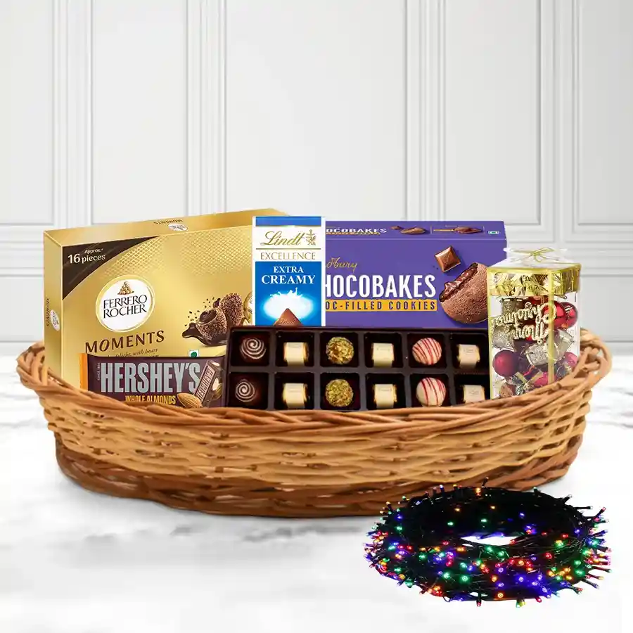 Christmas gift basket filled with assorted chocolates, festive decorations, twinkling lights, and a reusable cane basket.