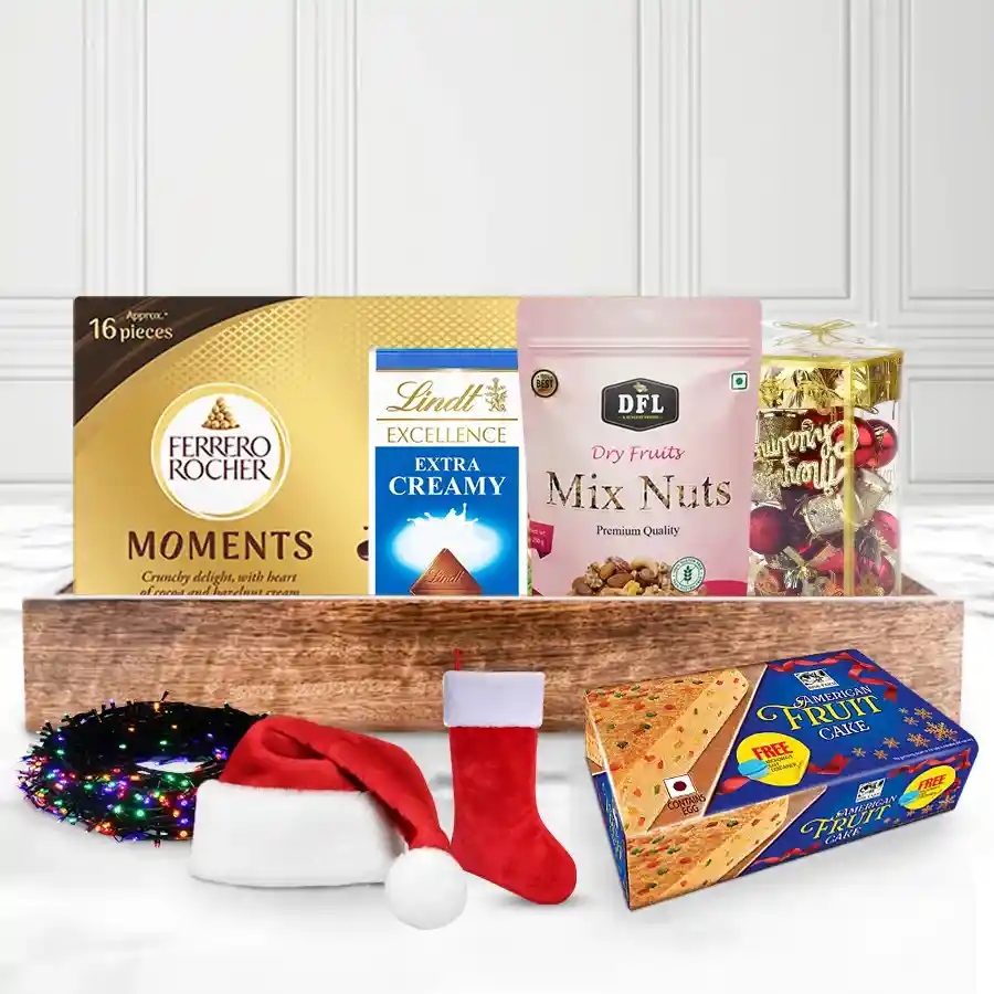 Tempting X-Mas Special Chocolate Gift Tray featuring American Fruit Cake, Lindt chocolates, mixed nuts, Ferrero Rocher Moments, and festive decorations on a wooden tray