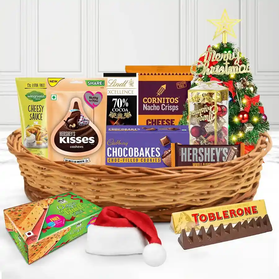Ultimate Gourmet Christmas Gift Basket filled with Toblerone, Hershey’s Kisses, Cadbury Chocobakes, Cornitos Nachos, Wingreens Cheesy Sauce, Lindt dark chocolate, a festive Christmas cake, decorations, a mini tree, and a stylish reusable basket.
