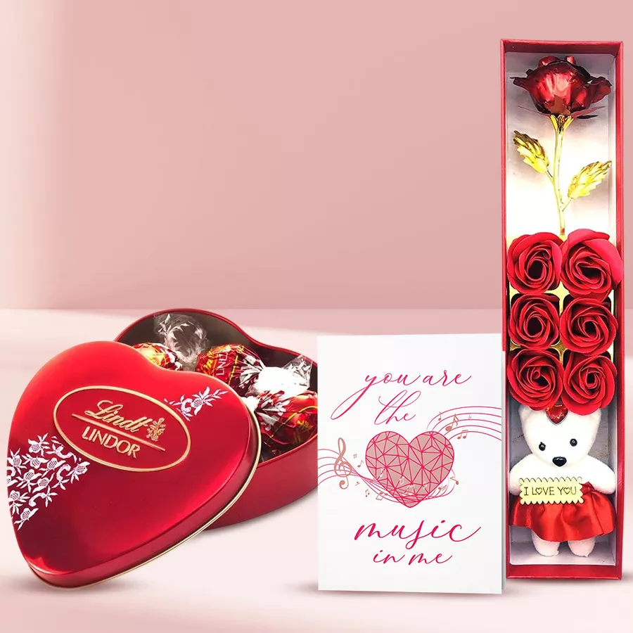 Magnificent bouquet of artificial red roses with a teddy bear, musical greeting cards, and Lindt Lindor chocolates arranged beautifully for a romantic gift.