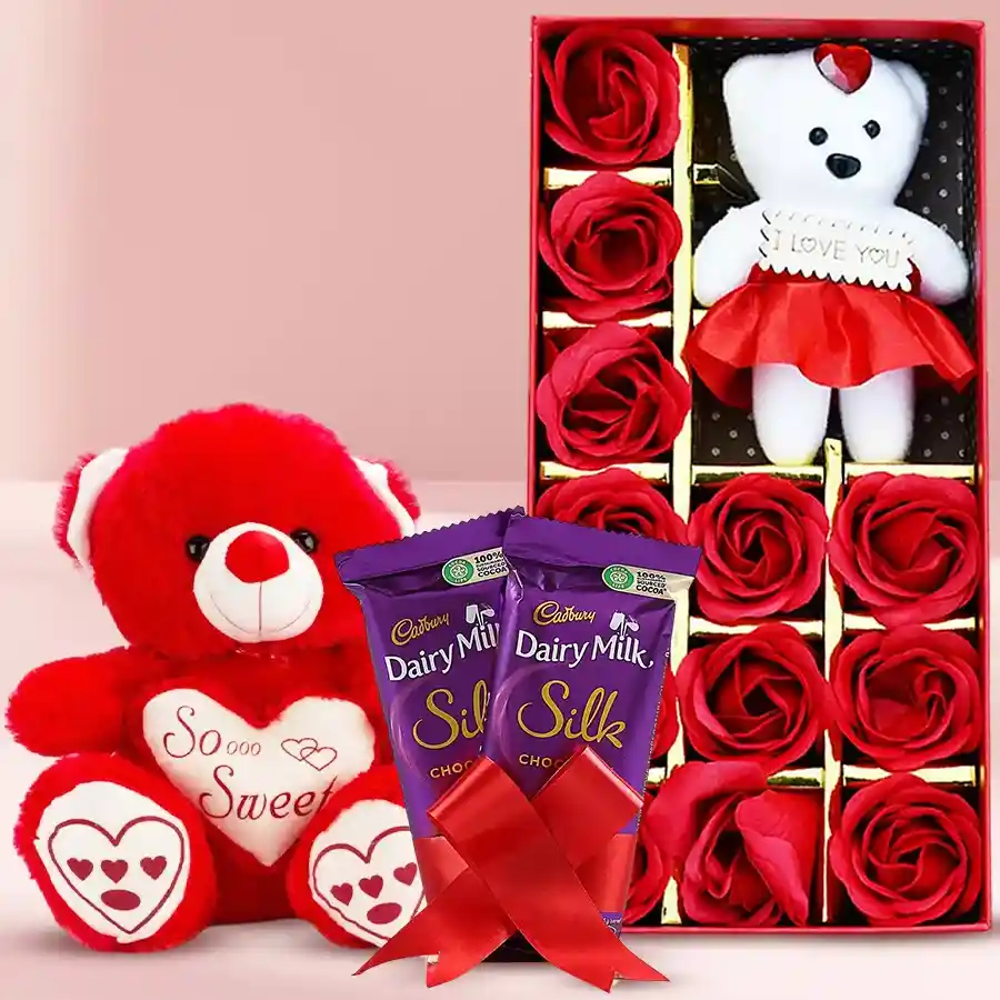 Valentine's Day gift assortment featuring artificial red roses, a teddy bear, Cadbury Silk chocolates, and a singing teddy bear
