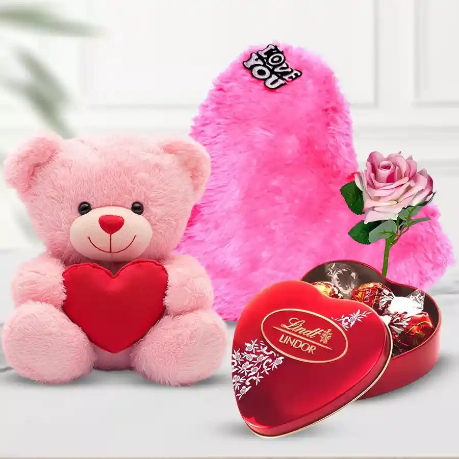 Valentine's Day gift combo featuring a pink teddy bear, Lindt Lindor heart-shaped chocolate box, pink heart-shaped cushion, and pink rose stick.