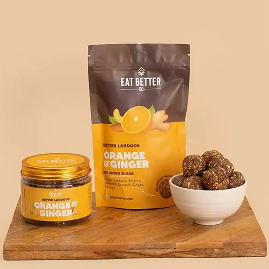 Premium Sugar Free Orange and Ginger Laddoos arranged on a wooden platter with nuts and oranges in the background.