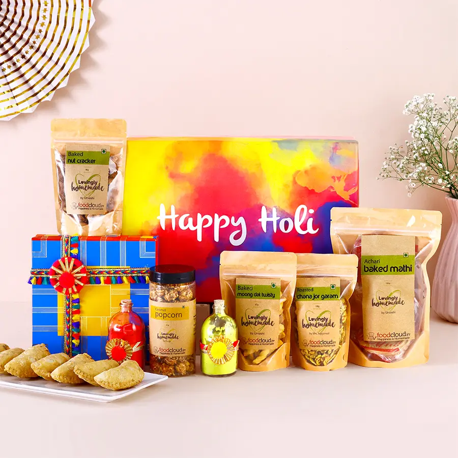 Tasty assorted treats for Holi celebration including baked Gujiya, Moong Dal Twisty, Caramel Popcorn, Nut Cracker, Roasted Chana Jor Garam, and jars of Organic Gulal.