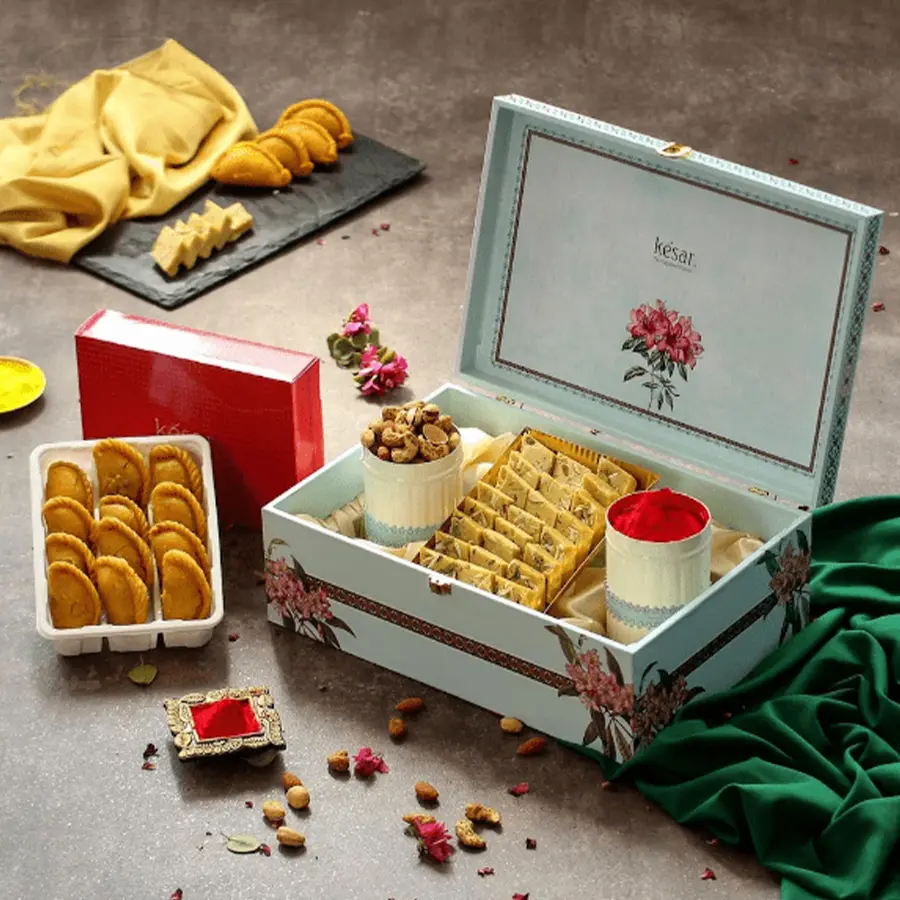 Vibrant gift box for Holi featuring organic colors, mixed nuts, thandai katli, kesar gujiya, and a greetings card.