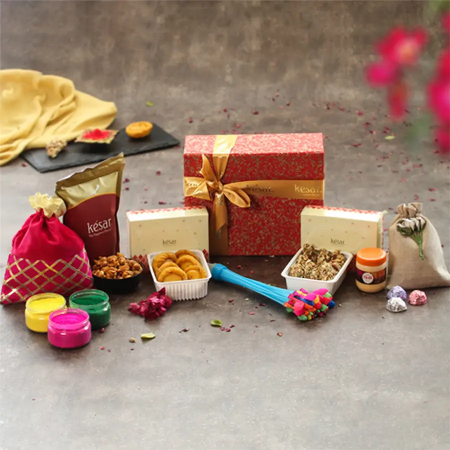 Colorful Holi Mega Gift Hamper featuring Dry Fruit Gujiya, Chandrakala, crunchy Peanuts, herbal colors, a water balloon, a pichkari with balti, premium chocolates, and a greeting card in a handmade paper box.