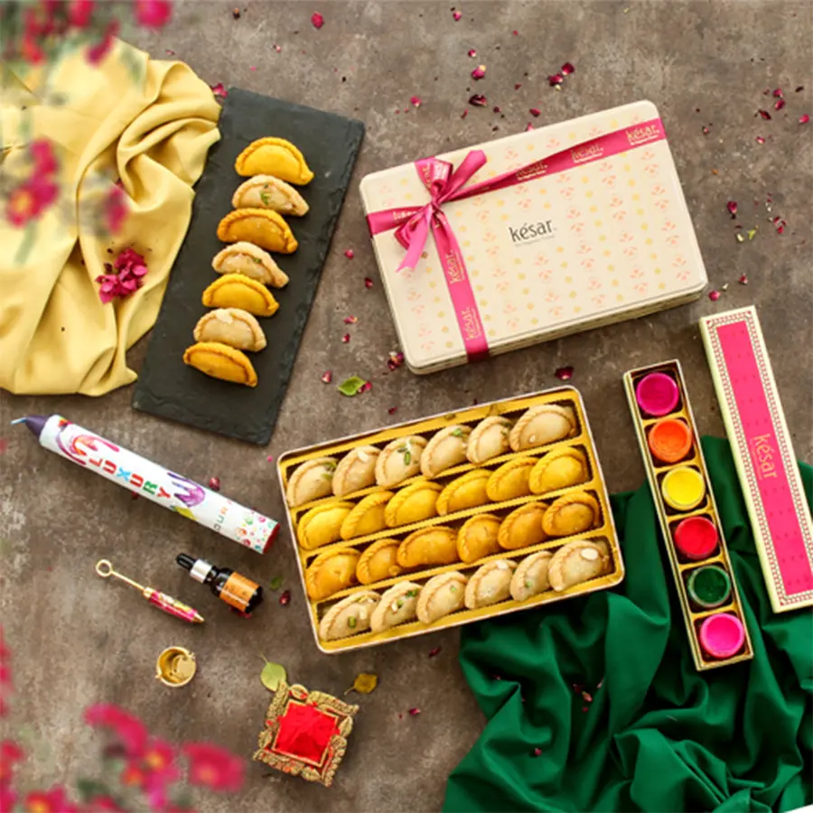 Premium Assorted Gujiyas and Holi assortments gift combo featuring colorful organic colors, Kesar, Plain, and Fikki Gujiyas, an essential oil, Holi balti with pichkari, and a cheerful greetings card in a vibrant corrugated box.