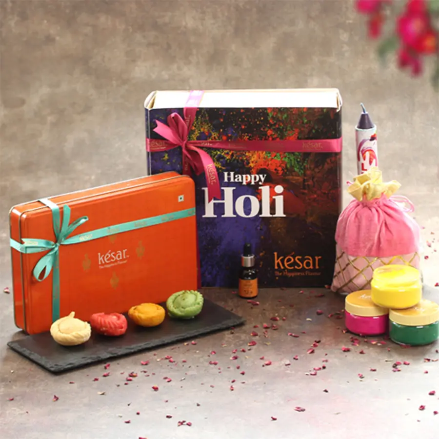 Delicious Assorted Chandrakala Gift Hamper with essential oil and Holi assortments including herbal colors, color bomb, pichkari, and greeting card in a vibrant package.