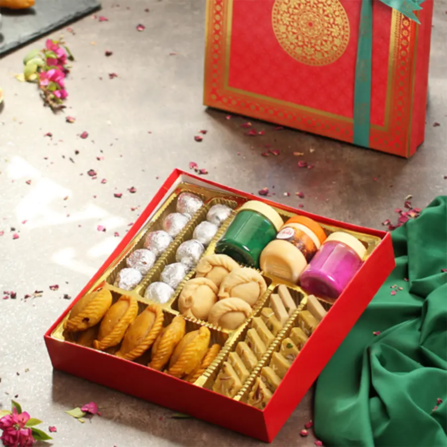 Holi gift hamper containing Chandrakala, organic colors, Chandan Jar, Kesar Gujiya, Thandai Katli, Dry Fruit Kachori, and a Holi greeting card in an elegant box.