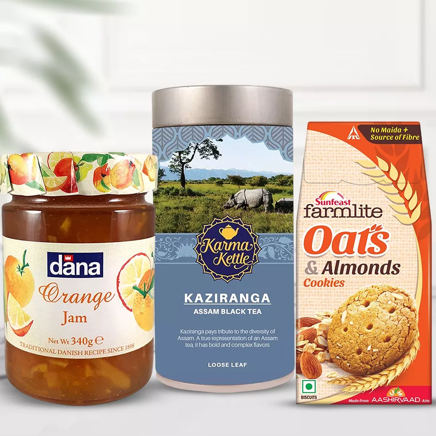 A beautifully arranged gift hamper featuring Authentic Kaziranga Tea, Farmlite Oats & Almond Biscuits, and Dana Jam, presented with a warm and inviting background.