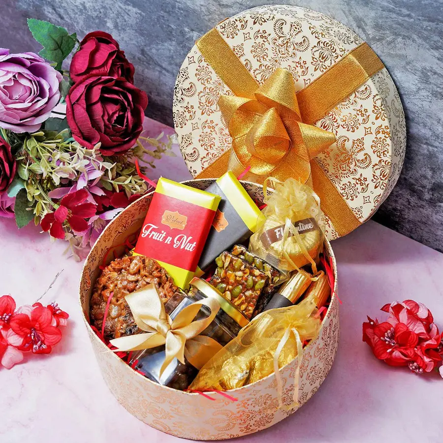 Sweet Golden Hamper for Mother's Day filled with chocolate bars, Florentines, almond rocks, and other treats in a festive round box.