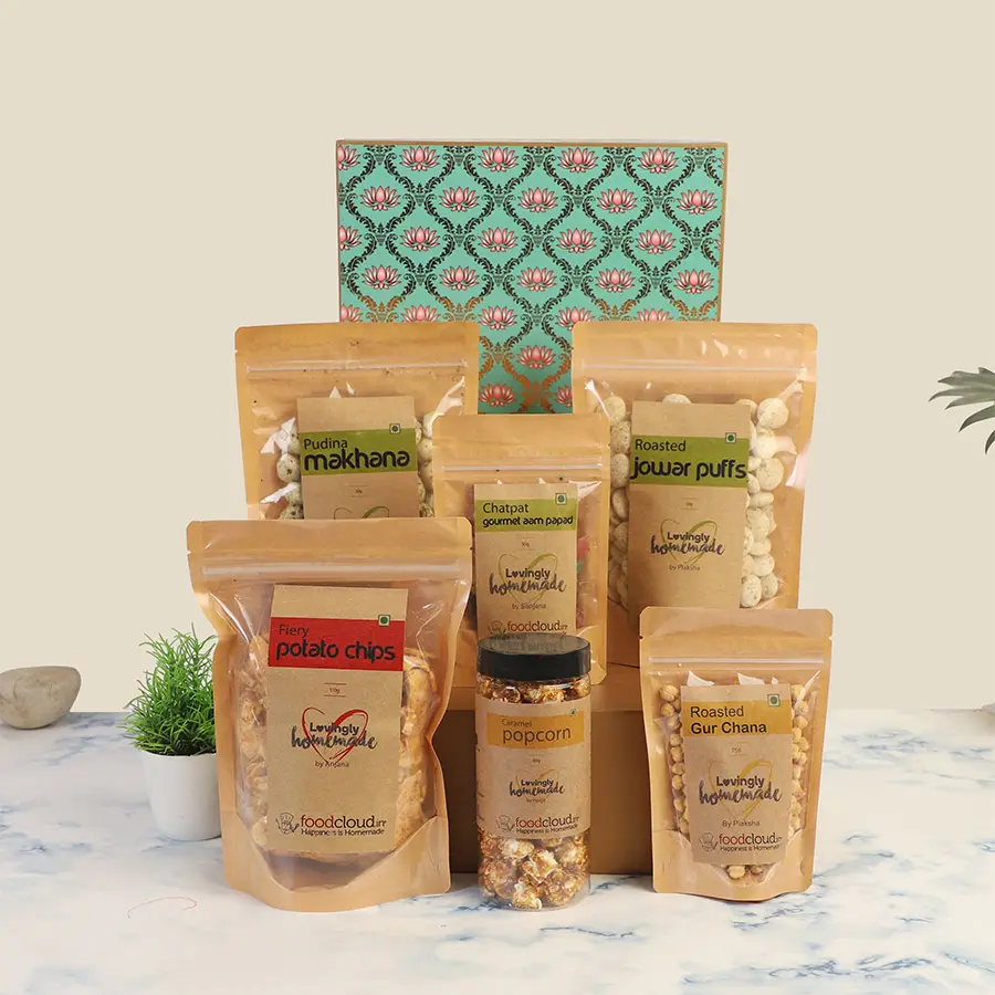 A colorful hamper filled with various gluten-free snacks including Roasted Gur Chana, Pudina Makhana, Fiery Potato Chips, Gourmet Aampapad, Roasted Jowar Puffs, and Caramel Popcorn, presented for a celebration.