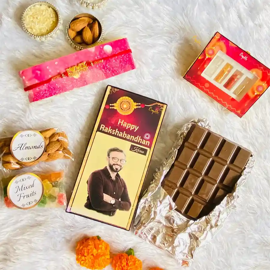 Customized Rakhi hamper with a red mauli rakhi, chocolate bar, dry fruits, roli tikka, and a greeting card.