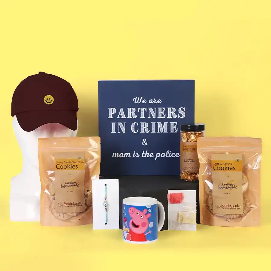 A colorful rakhi gift hamper featuring an Evil Eye Rakhi, Oats & Choco and Almond Cookies, caramel popcorn, a Peppa Pig mug, a trendy kids cap, and traditional roli chawal.