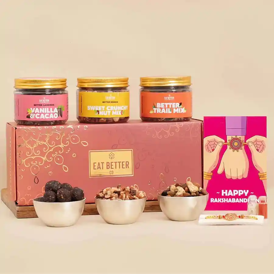 Handcrafted rakhi, three snack jars including sweet crunchy nut mix, vanilla & chocolate dry fruit laddoos, and premium nut mix, elegant glass bottles with roli tika and chawal, and a heartfelt greeting card in a beautifully arranged gift hamper for Raksha Bandhan.