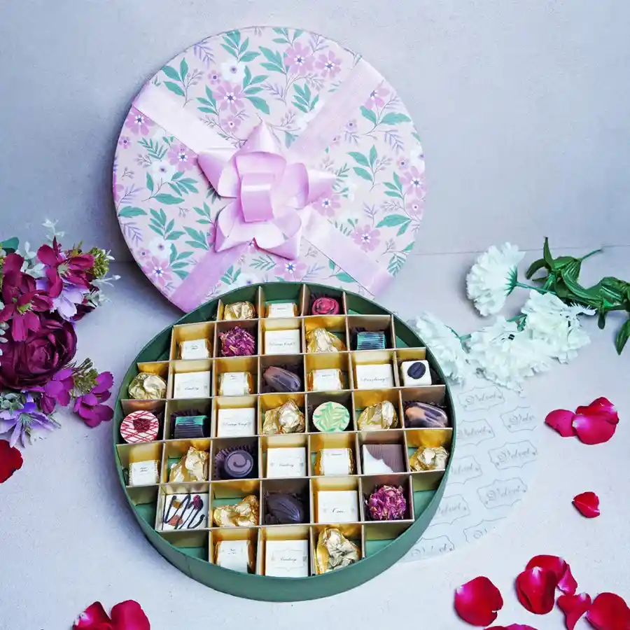 Festive Floral Box filled with 37 assorted chocolates in elegant round packaging, showcasing various flavors like Hazelnut, Coffee, Lemon, and Rose Truffles, designed for Raksha Bandhan celebrations.