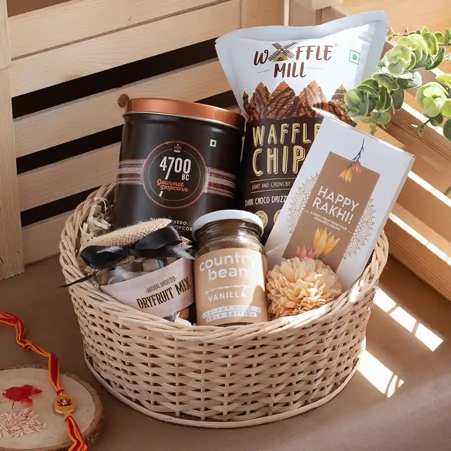Gourmet Delight Basket filled with gourmet chocolate popcorn, crispy chips, mixed dry fruits, vanilla instant coffee, a Happy Rakhi chocolate bar, and a Kundan Rakhi, elegantly arranged in a reusable round basket.