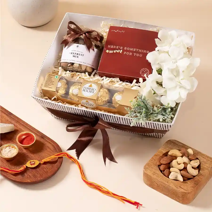Festive Gourmet Hamper featuring mixed dry fruits, handmade cookies, Ferrero Rocher chocolates, a reusable Kappy tray, a flower arrangement, and a Meenakari Rakhi.