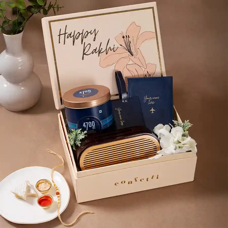 Travellers Delight Gift Hamper featuring a blue faux leather passport cover, luggage tag, Himalayan Salt Caramel Popcorn, wooden mobile sound amplifier, Spotify plaque, and a Rudraksh Rakhi in a Happy Rakhi beige box.