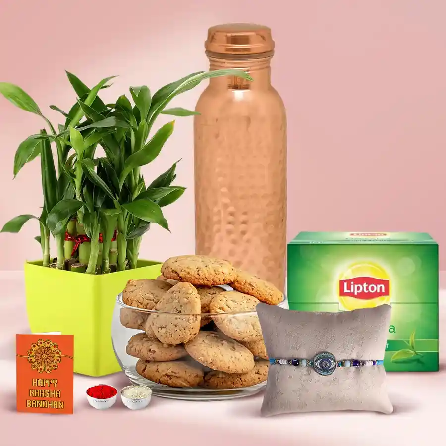 Greenery N Rakhi Treats Set featuring an Evil Eye Rakhi, a hammered copper bottle, a 2-tier bamboo plant, dry fruit cookies, a green tea diffuser with 10 tea bags, Roli Tika N Chawal, a personalized message card, and a free Rakhi.