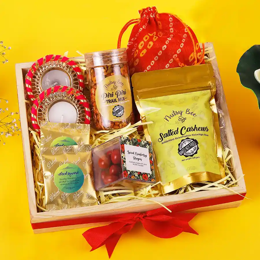 A festive hamper containing assorted chocolates, spicy trail mix, salted cashews, cranberry dragees, and two decorative diyas arranged beautifully.