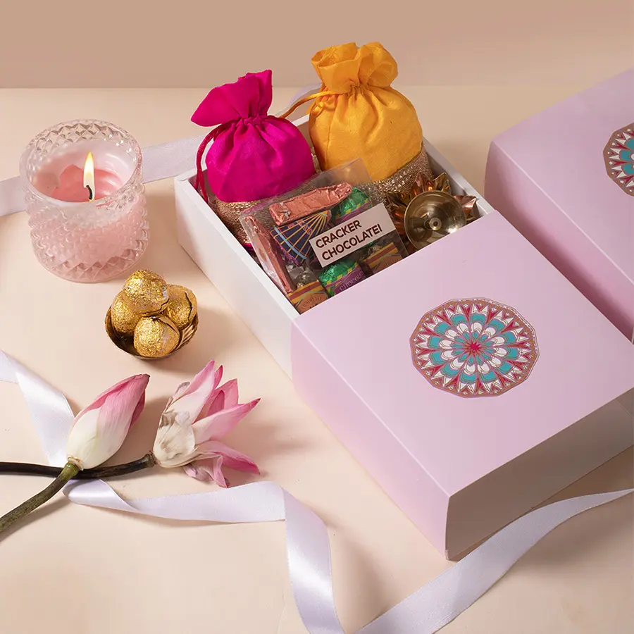 Diwali Brass Diya and Chocolate Collection featuring a pink potli with almonds, a yellow potli with cashews, and a decorative brass diya in a violet mandal box