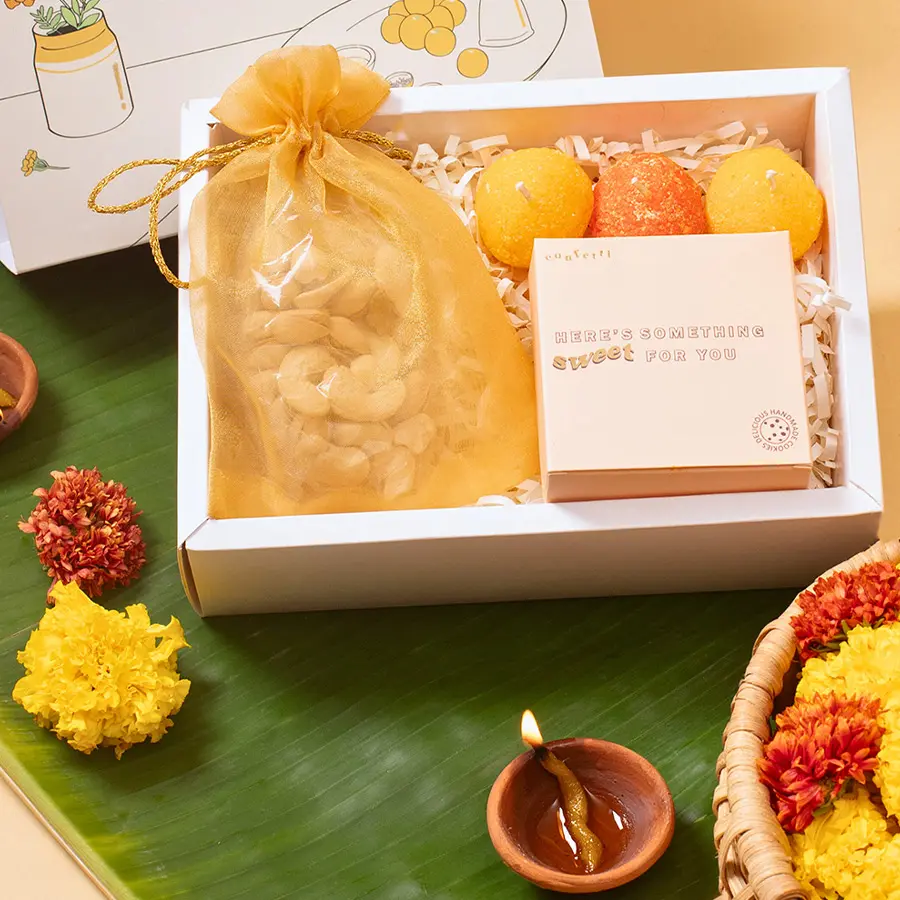 Diwali Sweets N Delights Trio Box featuring three Laddoo Candles, two Red Velvet Cookies, and a 100g organza potli of mixed dry fruits in an elegant Marigold Slider Box.