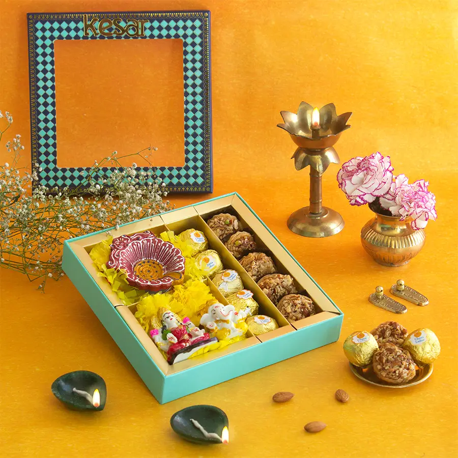 Elegant Diwali gift and sweets box featuring Chana Ladoo, Almond Tart Baklava, a Diya, a Ganesh Lakshmi idol, and a personalized greeting card in a stunning blue window box.