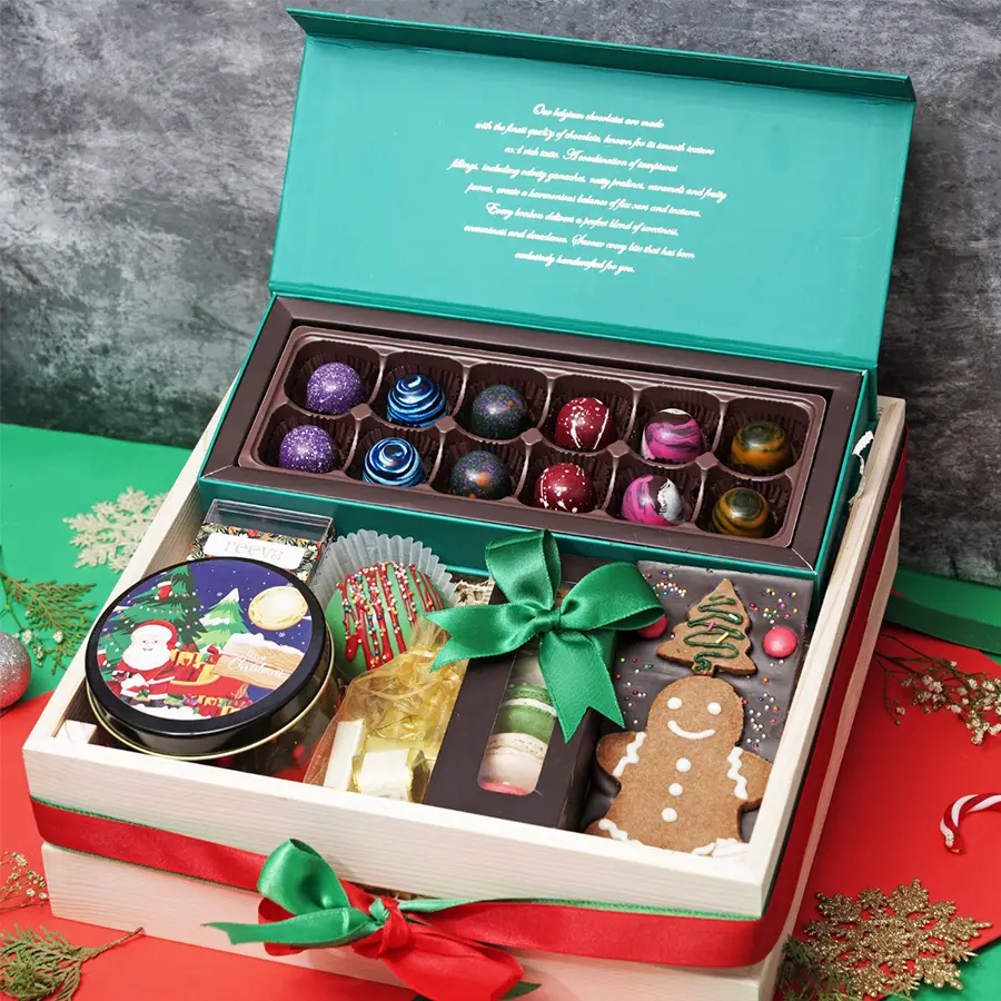 A beautifully arranged Christmas treats hamper featuring Belgian chocolate bon bons, a chocolate and cookie bar, colorful macarons, assorted chocolates, hot chocolate bomb, cranberry dragees, and snickerdoodle cookies, all set against a festive background.