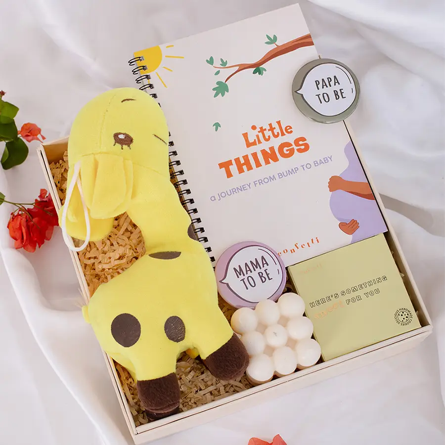 Delightful gift box for parents to be featuring a spiral journal, plush giraffe, badges, nut cookies, bubble candle, and black confetti box