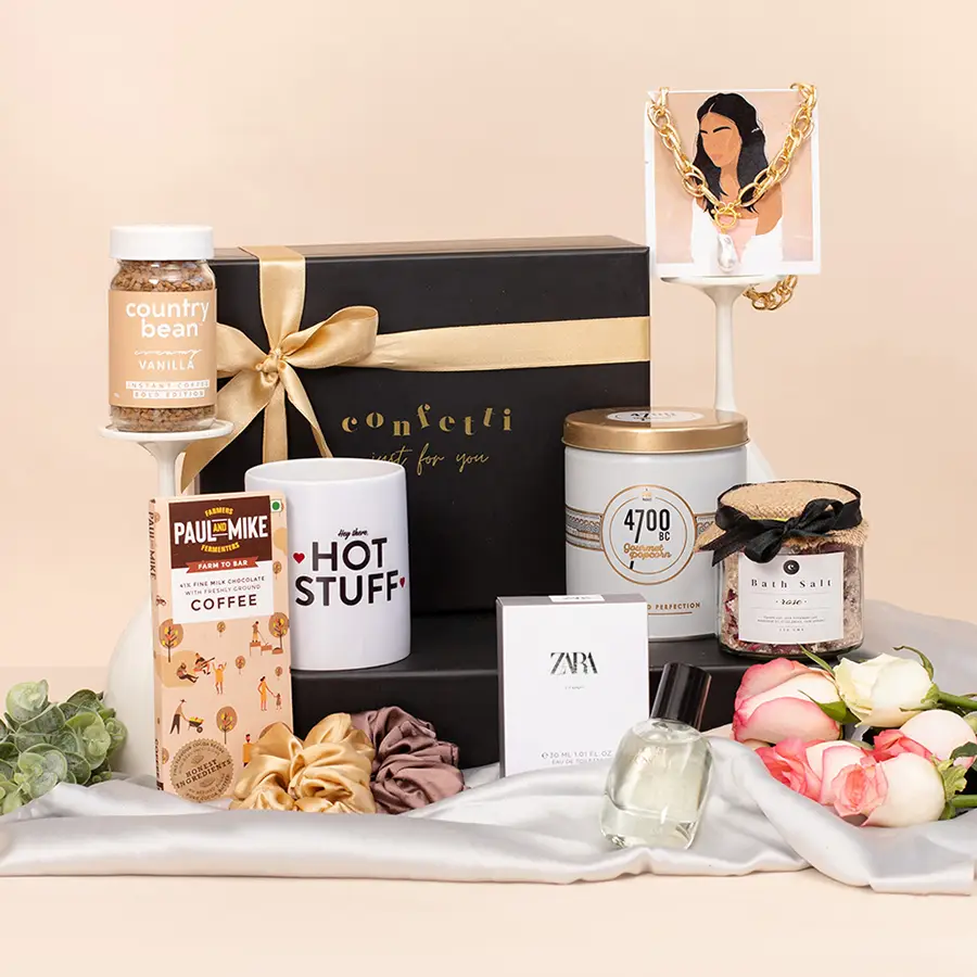 A luxurious gift box containing gourmet snacks, coffee, a pearl necklace, scrunchies, bath salt, chocolates, perfume, and a quirky mug.