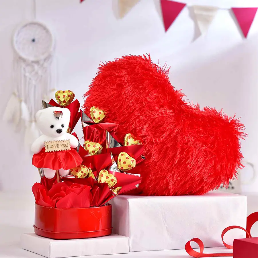 Red heart-shaped tin containing handmade chocolates, a cute doll, and a 10-inch red heart soft toy, arranged for Valentine's Day gift.