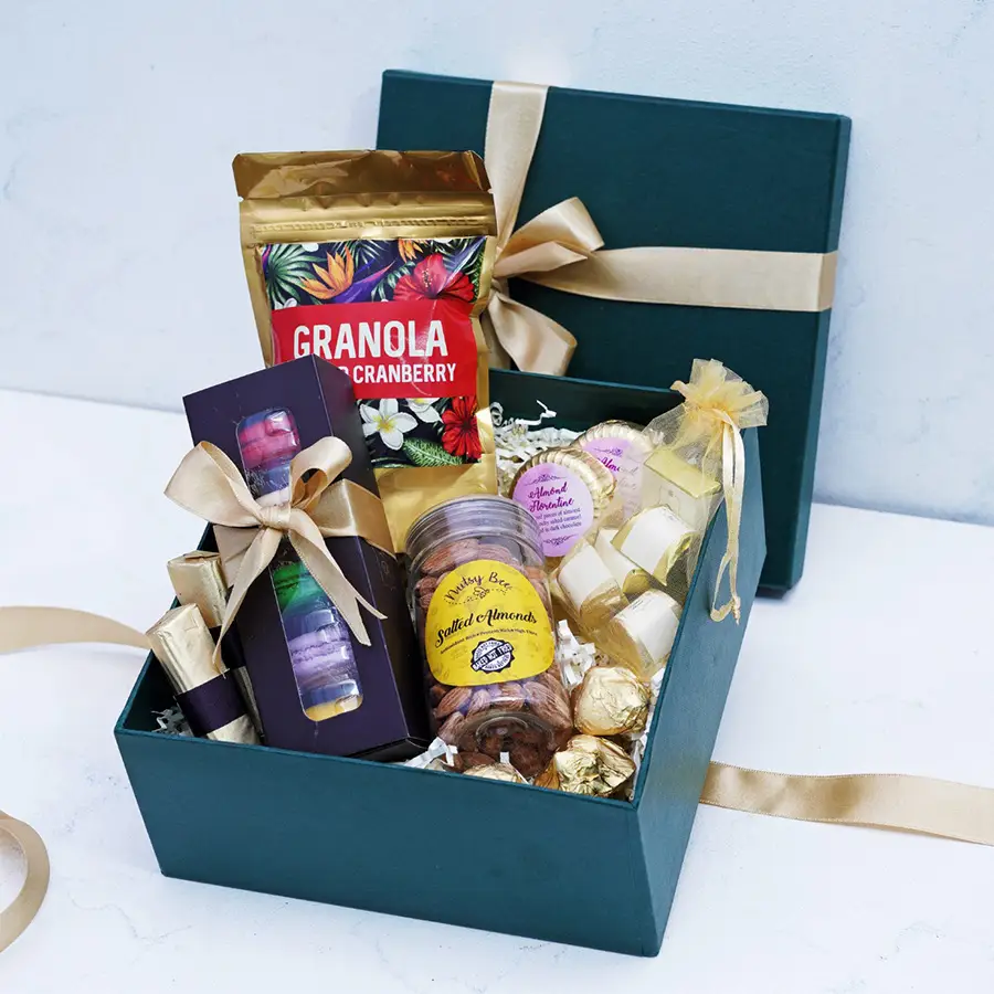 Delightful assortment of gourmet chocolates and treats including granola, chocolate logs, macarons, salted almonds, chocolate rocks, assorted chocolates, and Florentines displayed in an elegant box.