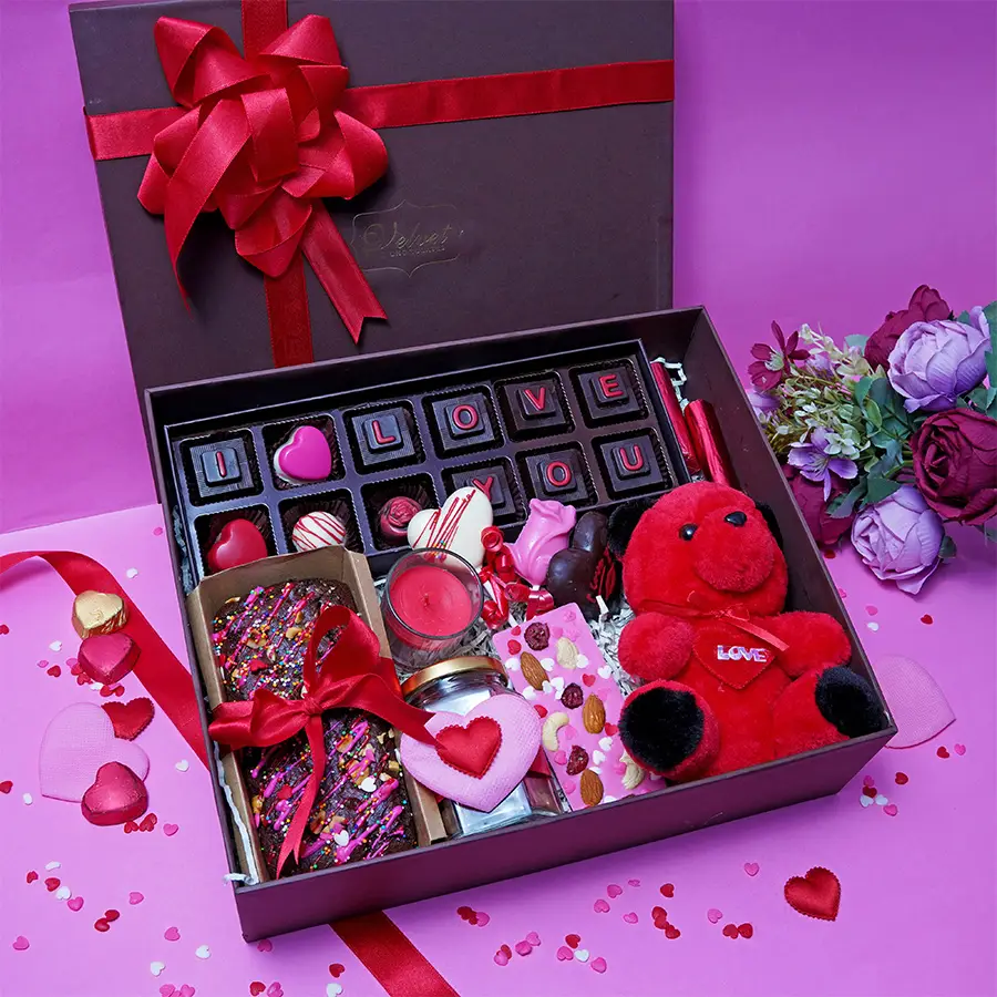 Cuddles N Chocolates Gift Hamper featuring assorted chocolates, fruit & nut bars, lollipops, a plush teddy bear, and a scented candle.