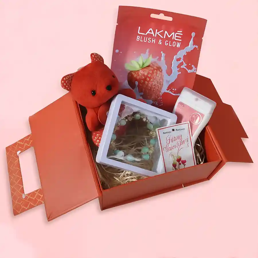 A beautifully arranged gift box containing a pendant necklace, a small red teddy bear, a pocket spray perfume, and a Lakme face mask, all designed for a delightful gifting experience.