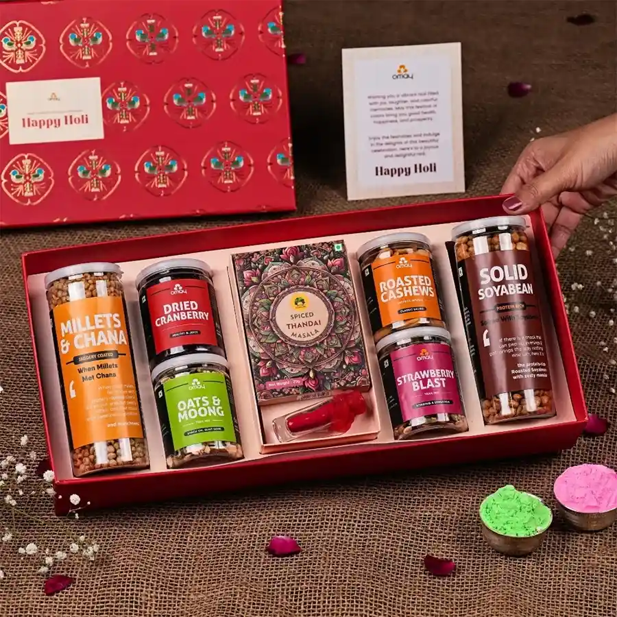 Exclusive Holi Healthy Treats Gift Box featuring jaggery-coated millets, roasted cashews, dried cranberries, Strawberry Blast Trail Mix, Gulab’s Instant Thandai, vibrant herbal gulal, and a cheerful Holi greeting card in a gold-foiled box.