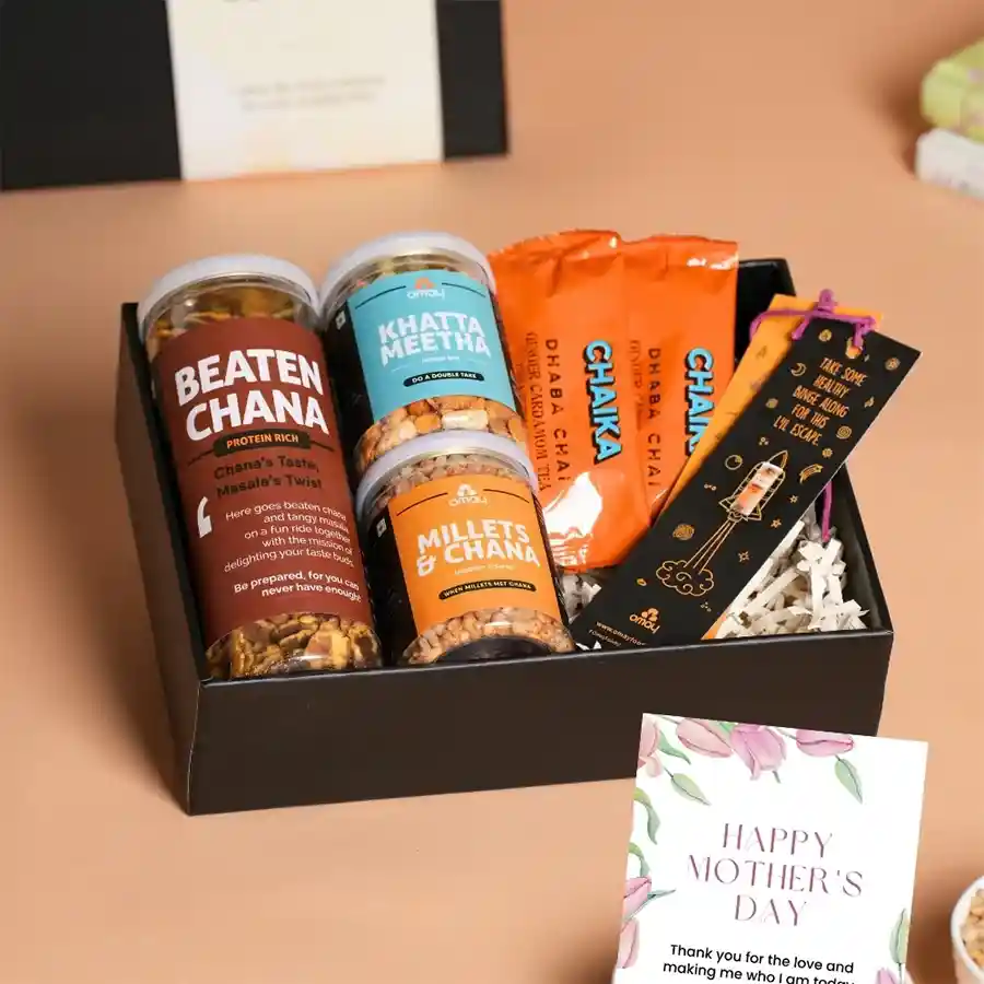 Elegant Mother's Day Gift Set featuring festive packaging, assorted snacks including Beaten Chana, Khatta Meetha, Millets & Jaggery Coated Chana, two packs of Dhaba Special Tea Mix, bookmarks, and a greeting card.