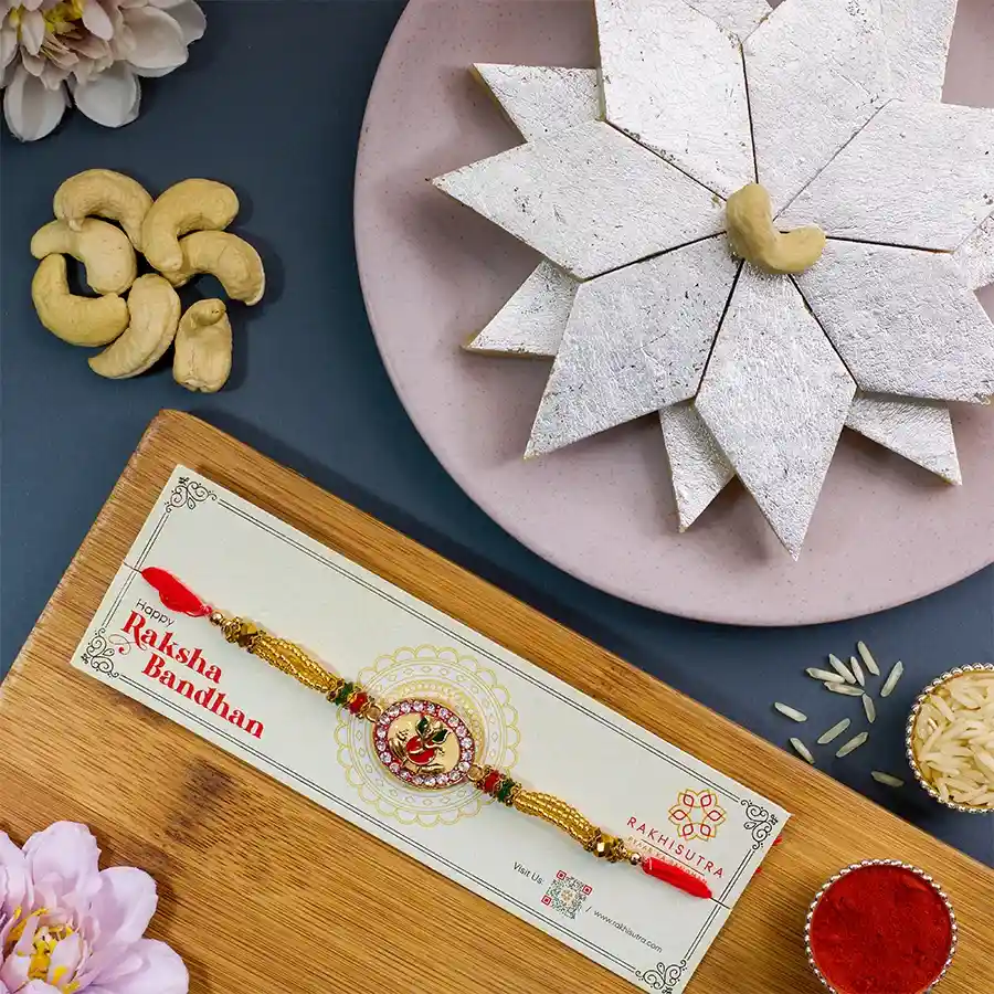 Divine Ganesha Rakhi with Kaju Katli, Roli Tika, Chawal, and message card in a festive arrangement