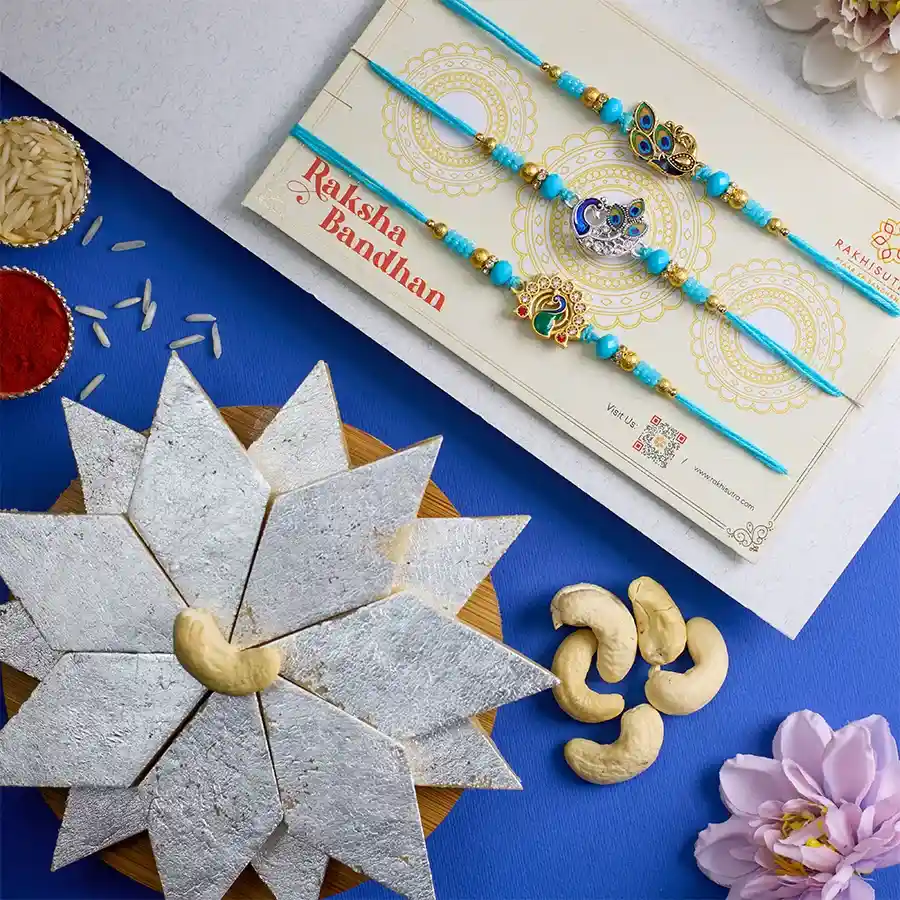 Beautiful Peacock Rakhi set with three elegant Rakhis, a 250g box of Kaju Katli, and traditional Roli, Tika, and Chawal for Raksha Bandhan celebration.