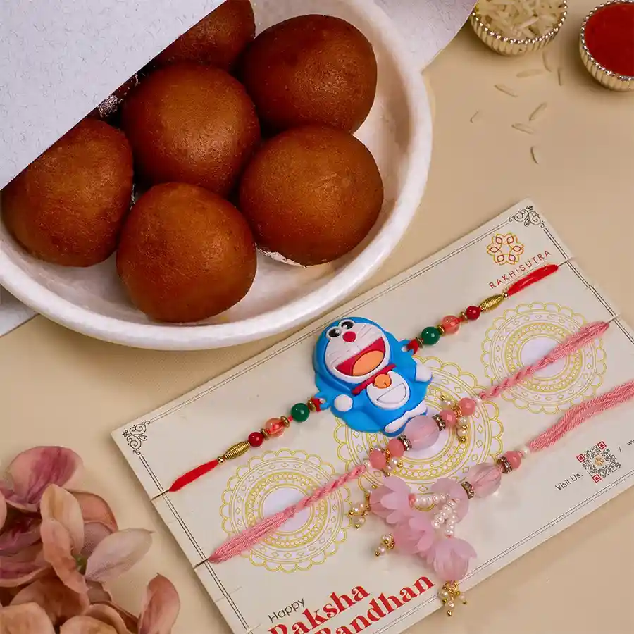Fancy Family Rakhi Set featuring Bhaiya Bhabhi Rakhi, Kids Doraemon Rakhi, and 500g of Gulab Jamun, with complimentary Roli Tika, Chawal, and a free message card.