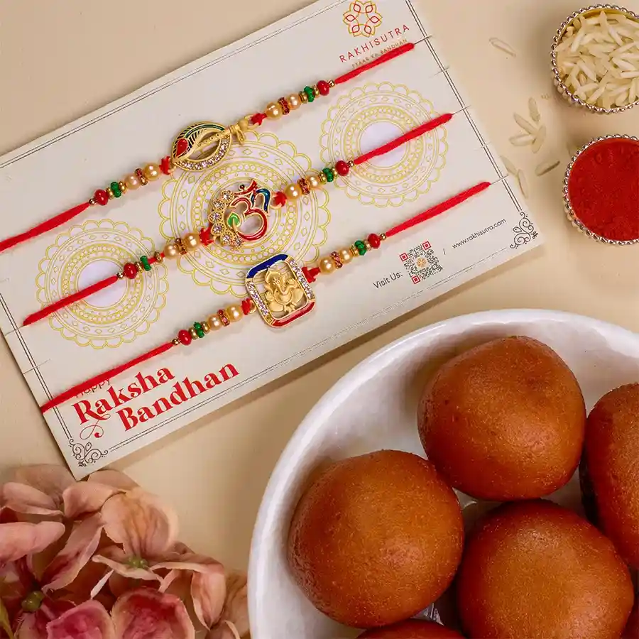 Festive Rakhi set featuring three Rakhis with Om, Ganesh, and Krishna flute designs, accompanied by a box of Gulab Jamun and Roli, Tika, and Chawal for celebration.