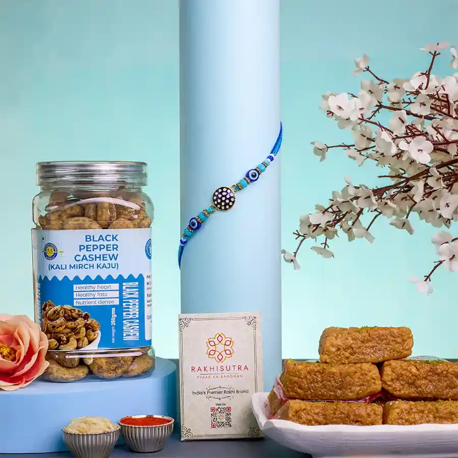 Protective Rakhi with Evil Eye design alongside a Mini Milk Cake and a jar of Black Pepper Cashews, accompanied by Roli, Tilak, Chawal, a heartfelt message card, and an extra free Rakhi.