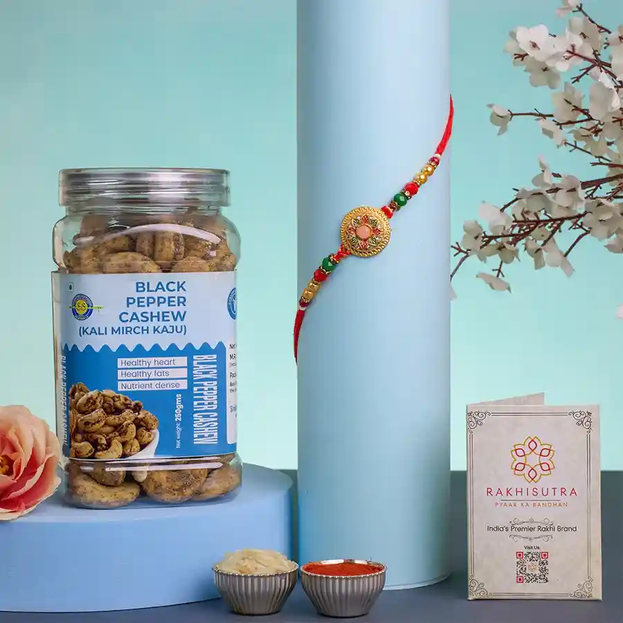 Elegant Kundan Rakhi with gourmet treats including Mini Milk Cake and Black Pepper Cashews, accompanied by Roli, Tilak, Chawal, and a personalized message card