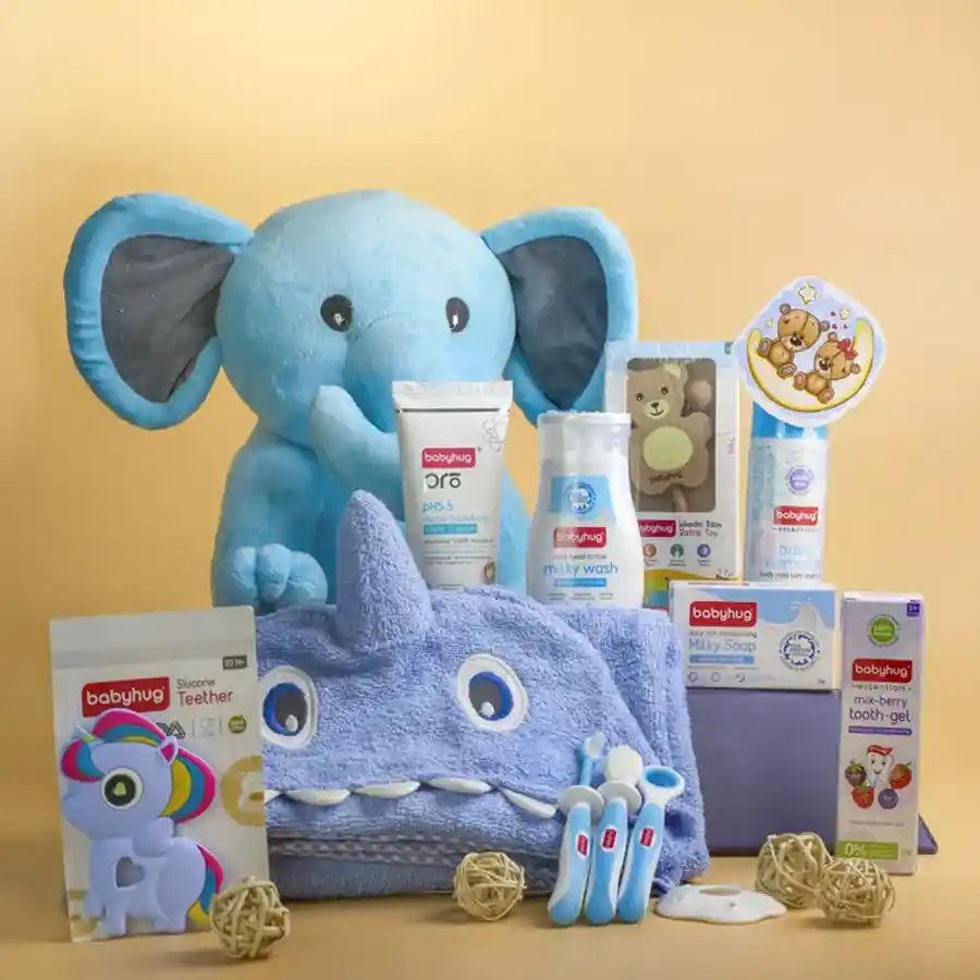 Newborn Comfort N Play Gift Set featuring a cuddly elephant plush, soothing body mist, Babyhug moisturizers, a soft wrapper blanket, a wooden rattle, a silicone teether, and oral care essentials arranged in a stylish basket.