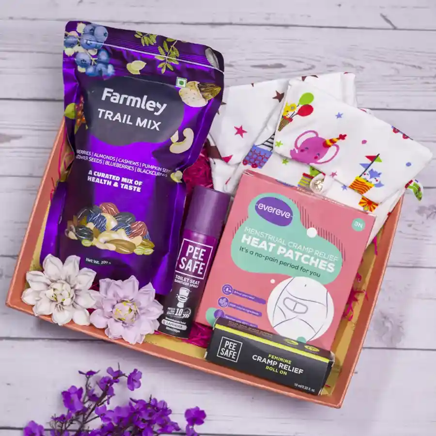 Essential Care N Comfort Kit featuring a toilet sanitizer, feminine cramp roll-on, heat patch, sanitary pad pouches, and trail mix in a designer tray.