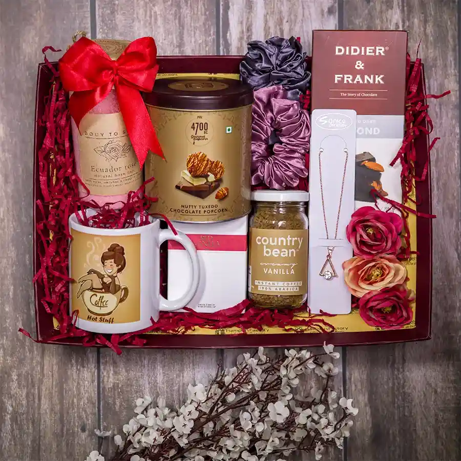 Indulgent Relaxation Bundle featuring gourmet nutty chocolate popcorn, roasted dark almonds, vanilla instant coffee, rose bath salts, Hot Stuff mug, stone-studded necklace, Zara Red Vanilla perfume, and a reusable designer tray.