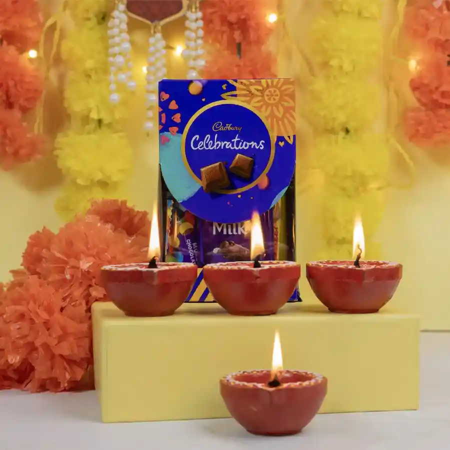 Cadbury Chocolates in a decorative box alongside four colorful mud diyas on a festive background