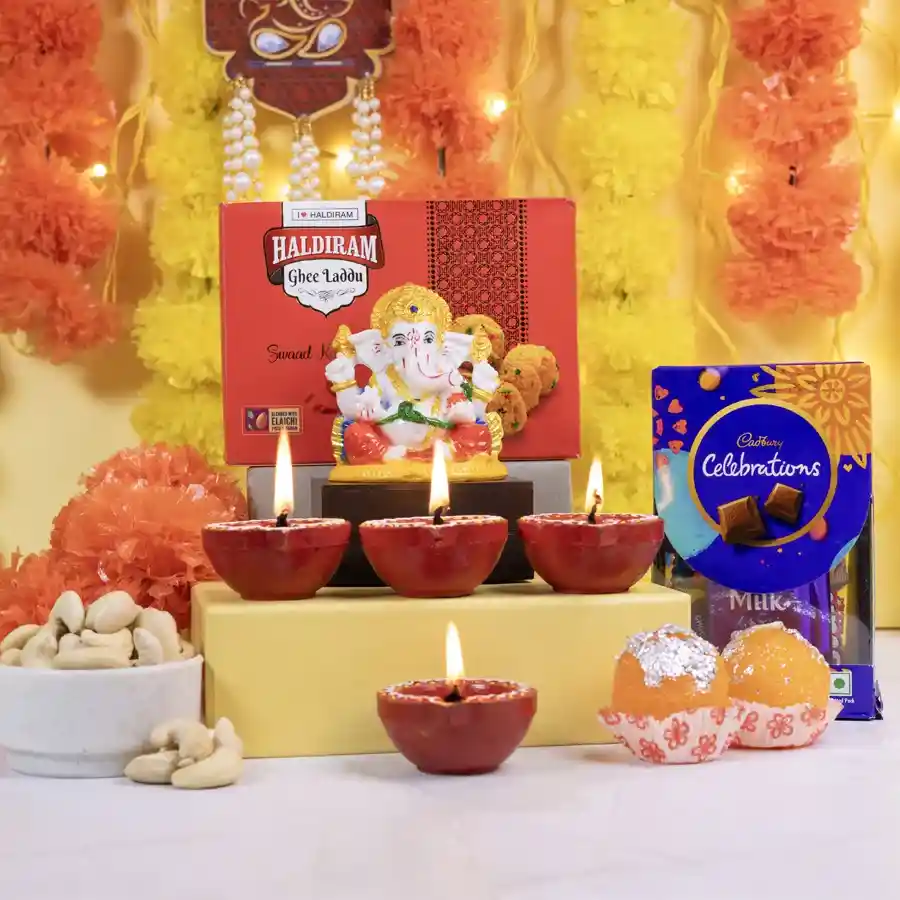 A beautifully arranged gift set featuring a Marble Abhaya Mudra Ganesha statue, Ghee Laddus, Cadbury Celebrations chocolates, Mud Diyas, Laddu Candles, and roasted cashews, all set against a festive backdrop.