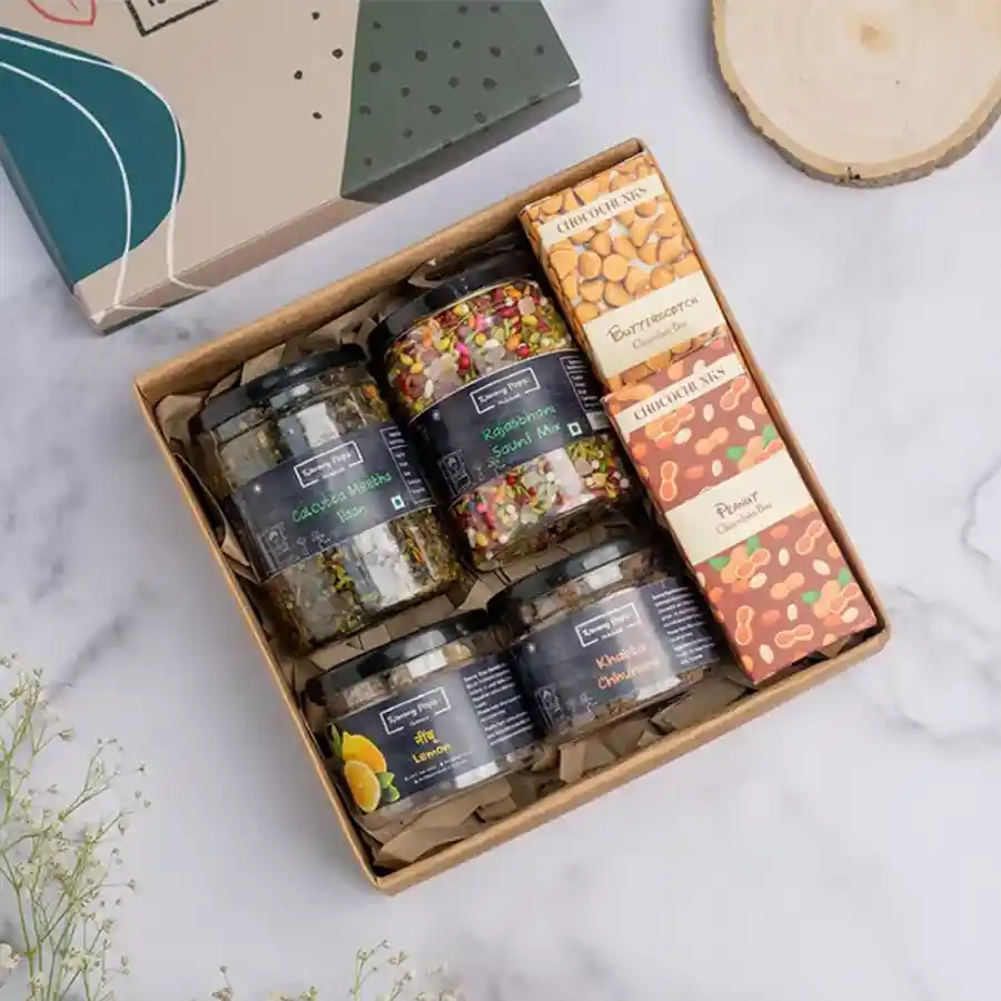 A beautifully arranged gift pack featuring assorted mukhwas and chocolate bars, showcasing flavors like Calcutta Meetha Paan and Rajasthani Saunf, alongside butterscotch and peanut chocolates, all presented in an elegant packaging.