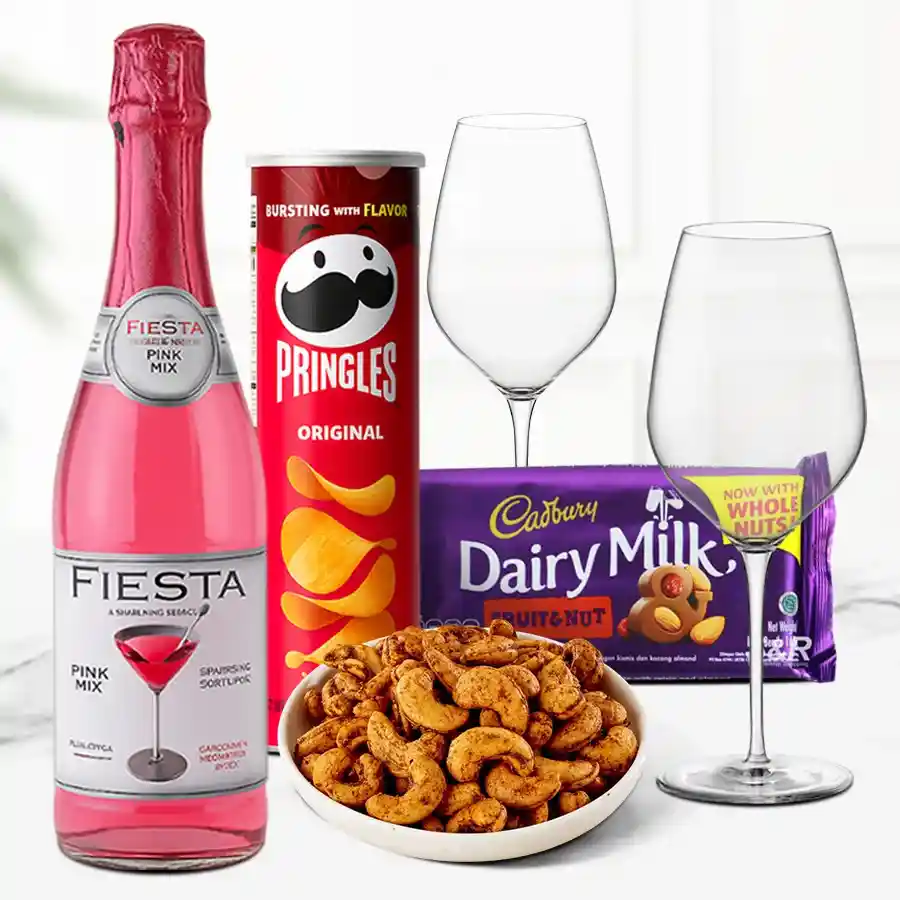 A beautifully arranged Christmas hamper filled with Masala Cashew Nuts, Pringles Chips, Cadbury Dairy Milk Fruit & Nut chocolate, a bottle of sparkling Fiesta Fruit Juice, and two elegant wine glasses, showcasing festive cheer and holiday treats.